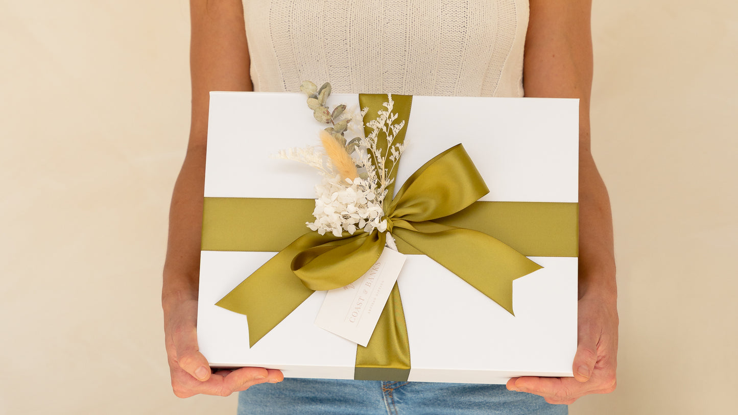 Gift box with a green ribbon held by a person against a beige background