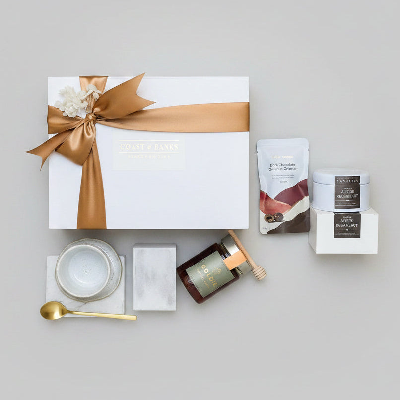 Gourmet gift set with a candle, chocolate, and tea on a wooden surface.