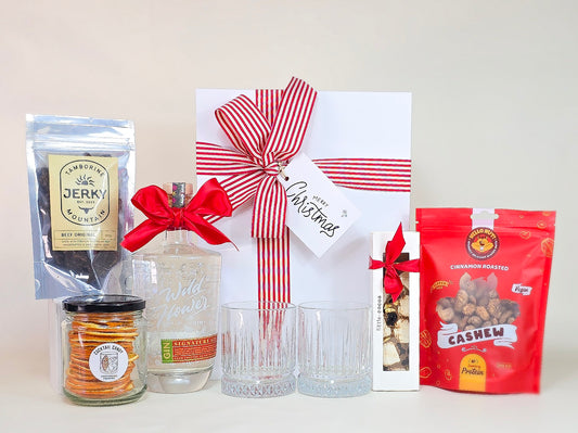 Gift set with a bottle of gin, a box with a red ribbon, and various snacks on a white background