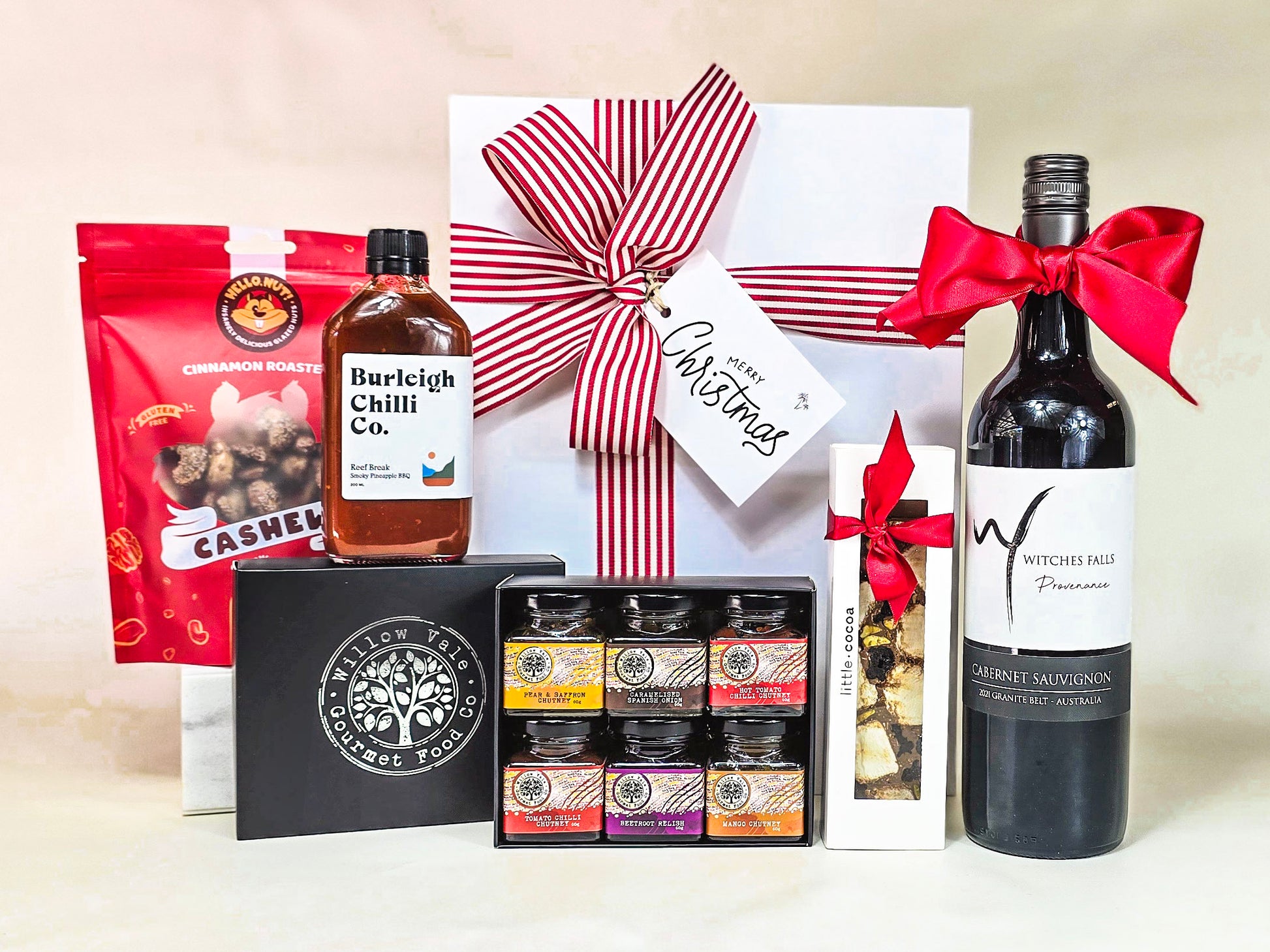 Gift basket with a bottle of wine, snacks, and other items on a beige background