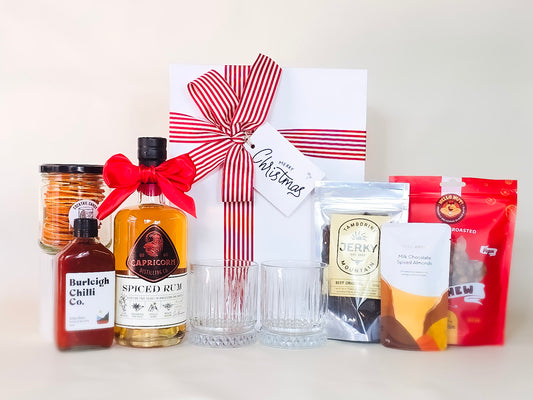 Gift set with a bottle of spiced rum, a jar of chilli, a pack of jerky, and a box with a red ribbon on a white background.