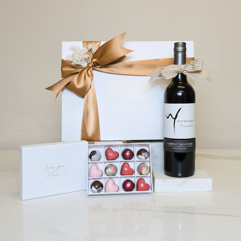 Wine bottle, chocolates, and gift box on a wooden surface with a beige background