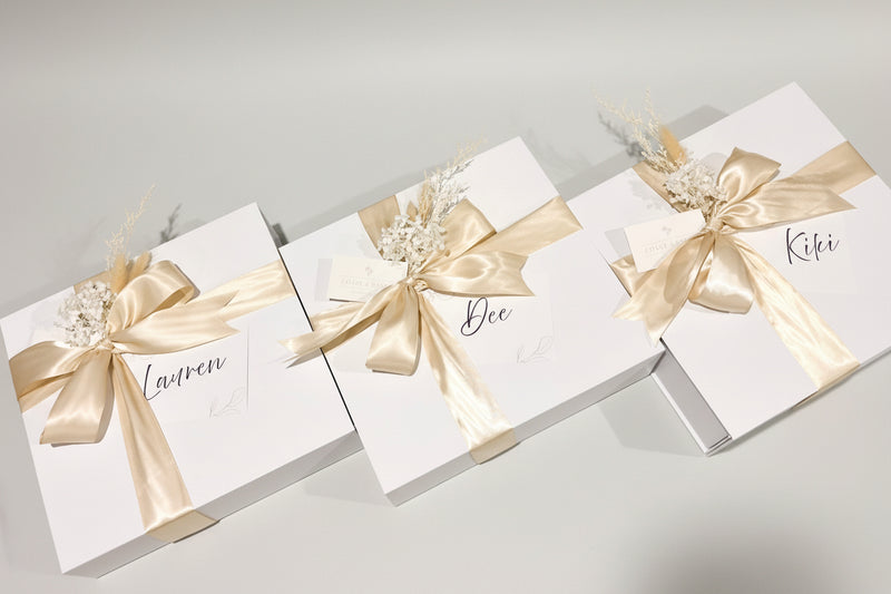 Three white gift boxes with gold ribbons and names on a wooden surface